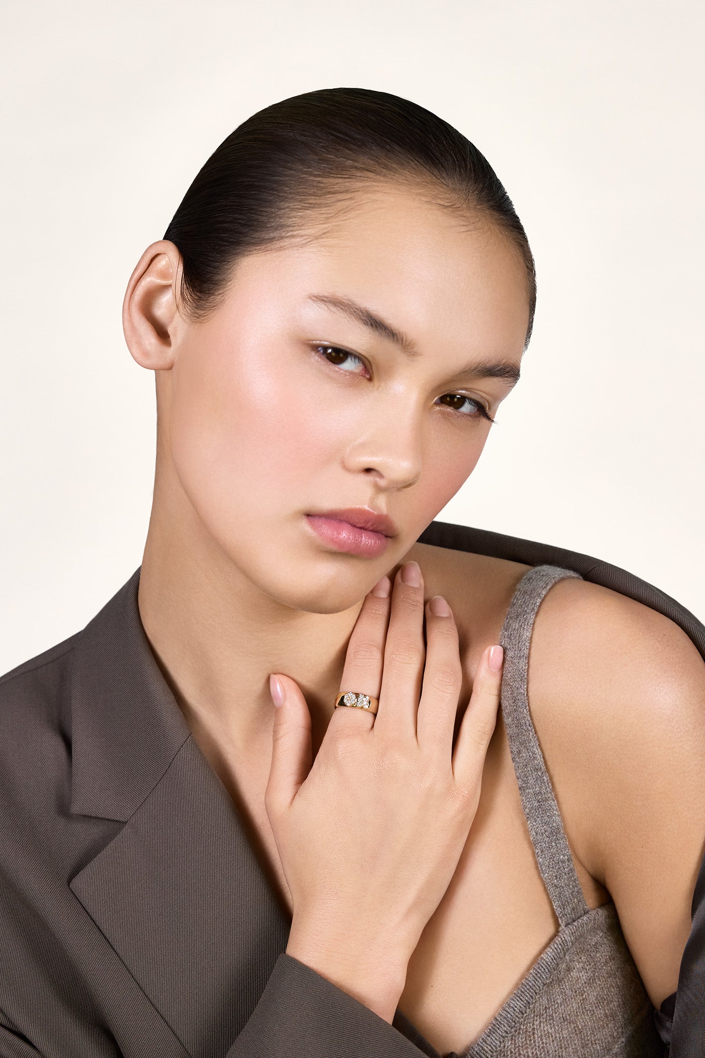 A young woman wearing a brown blazer and showing her shoulder. She is wearing a gold band with the letters "OK" on it, embellished with moissanites.