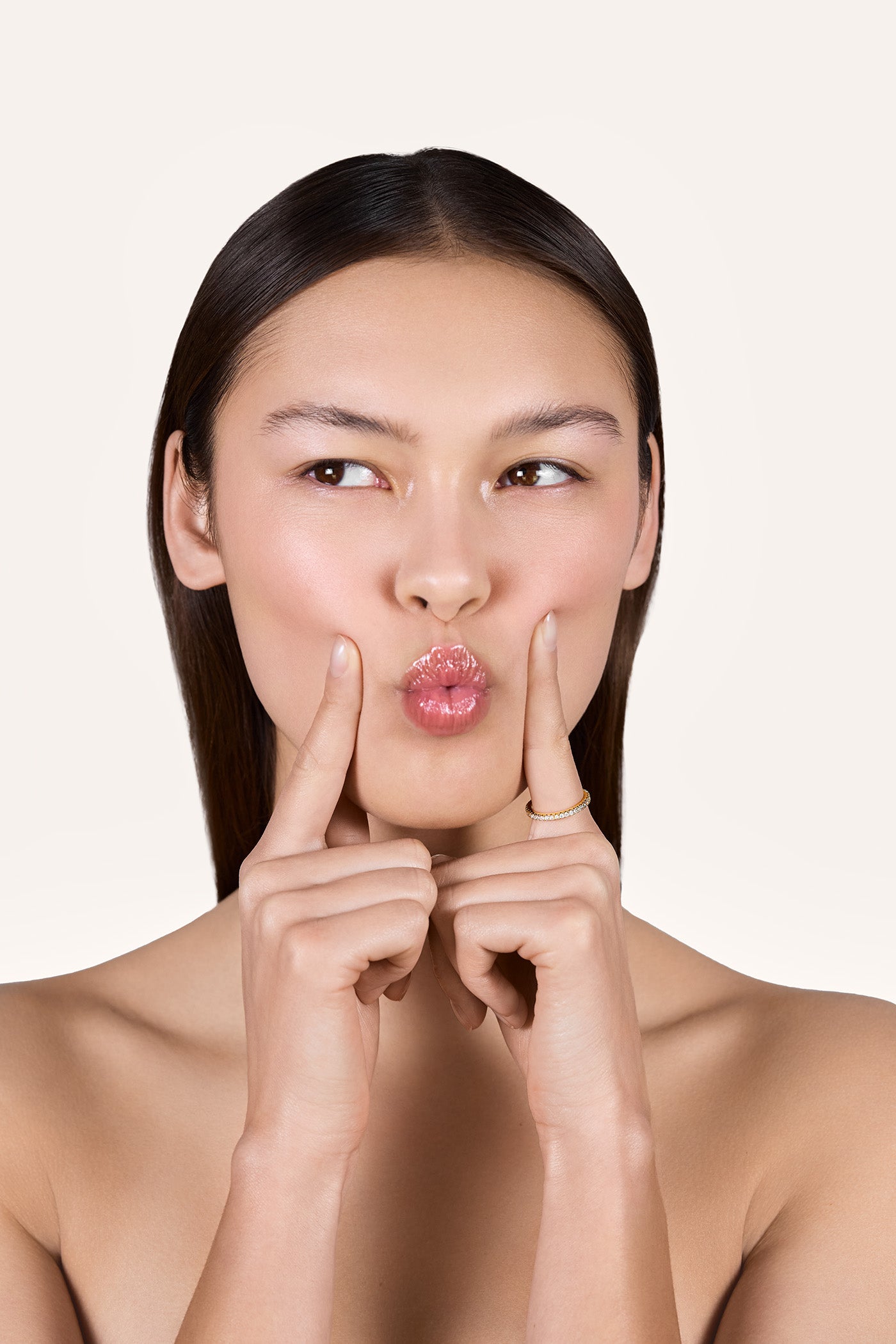 A young woman puckering her lips while holding her two index fingers beside her mouth, with one finger wearing the Eliana 2mm Eternity Ring featuring lab-grown diamonds