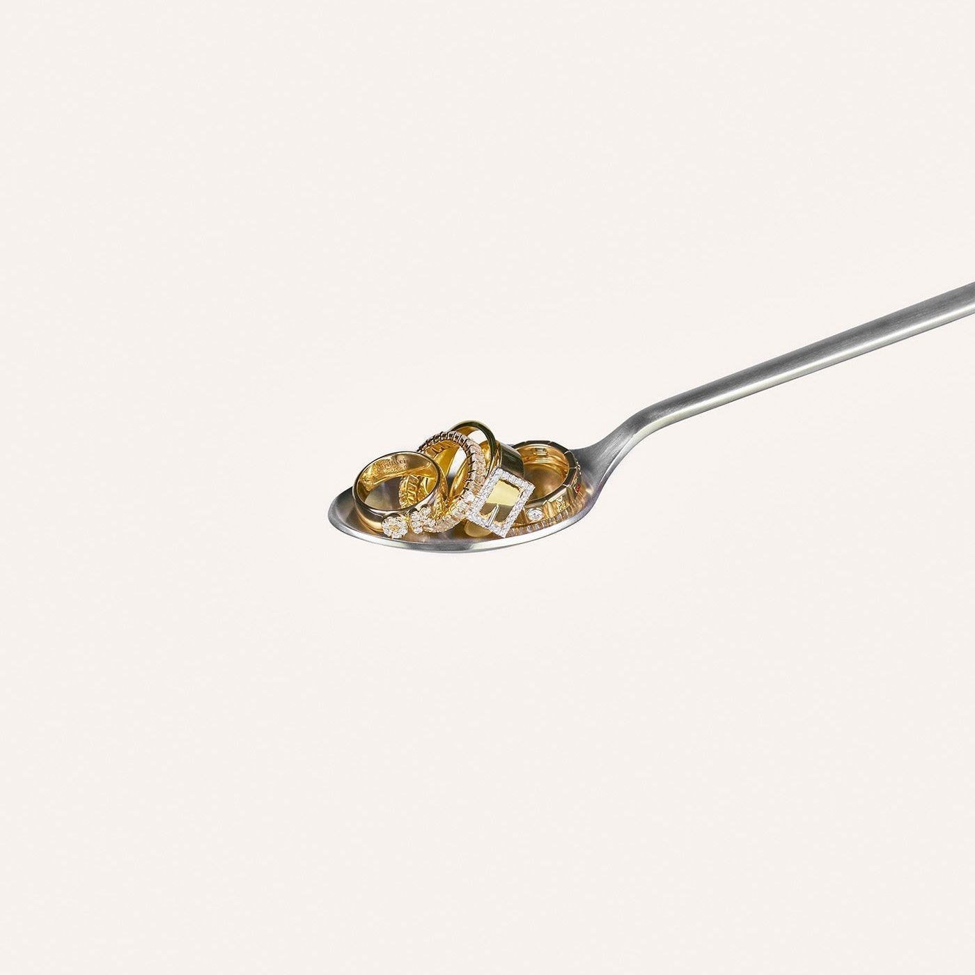 A silver spoon with five solid gold rings resting on it.