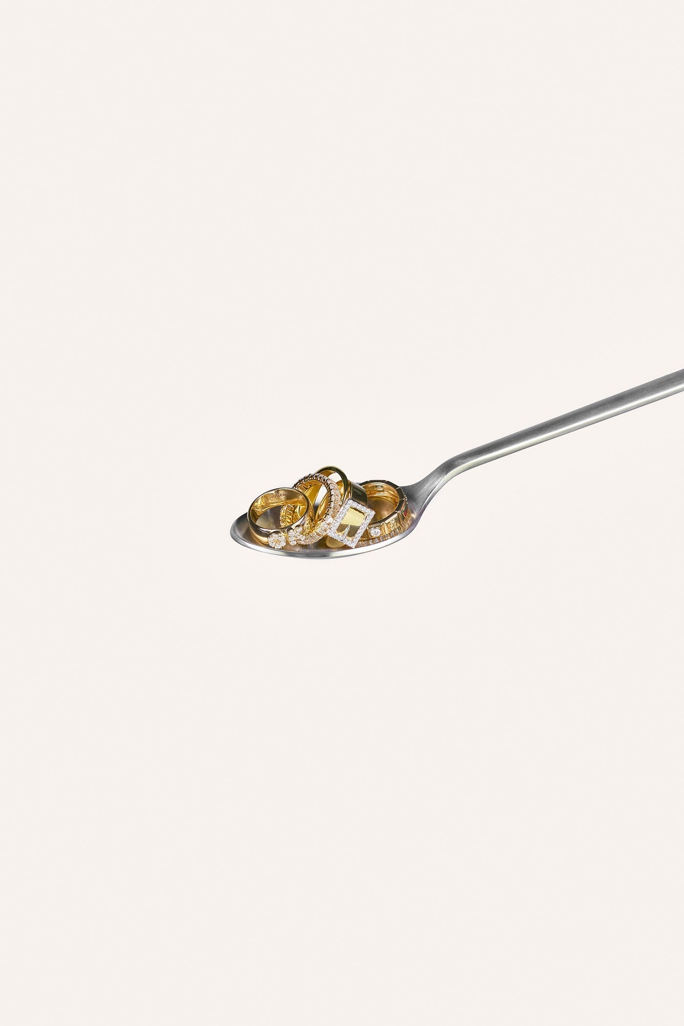 A silver spoon with five solid gold rings resting on it.