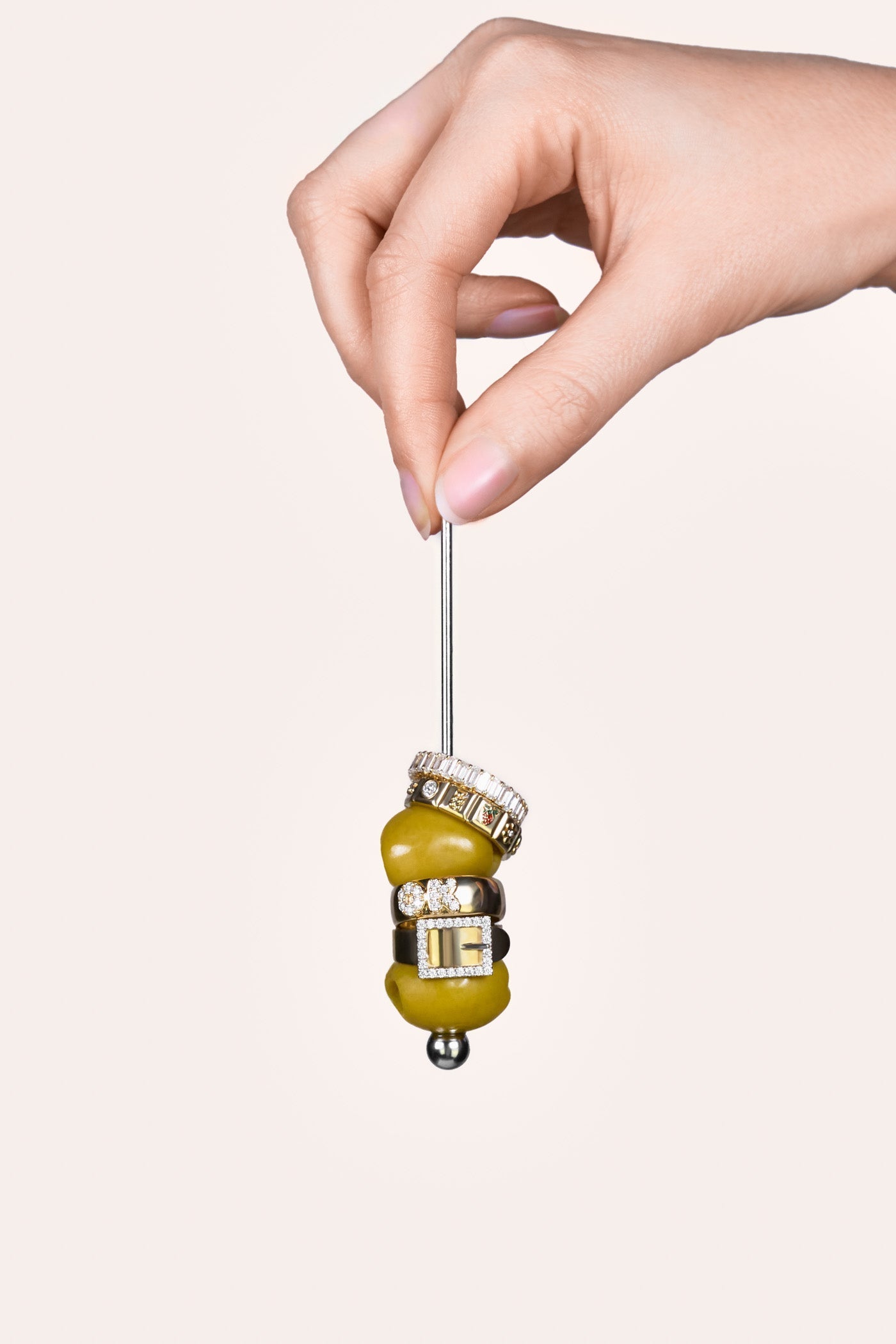A woman's hand holding a silver cocktail stick, with two stacked rings, followed by an olive, then two rings and another olive.