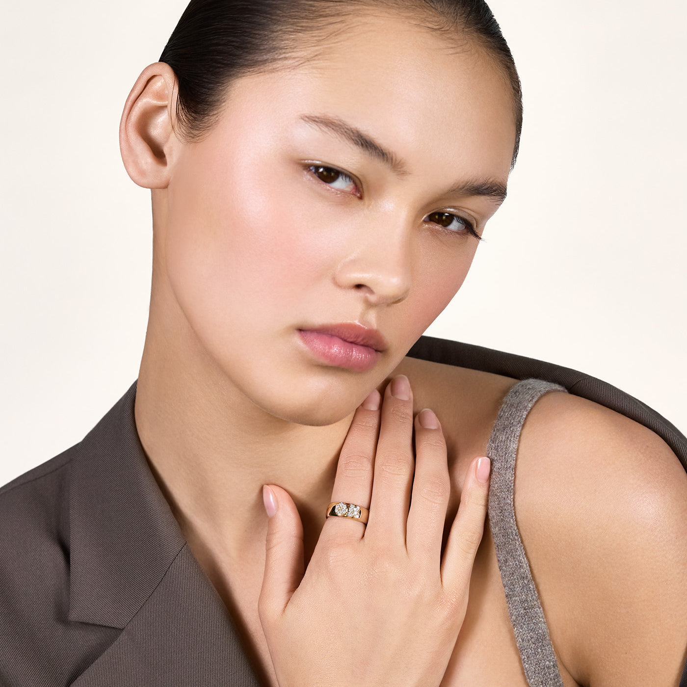 A young woman wearing a brown blazer and showing her shoulder. She is wearing a gold band with the letters "OK" on it, embellished with moissanites.