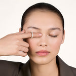 A young woman wearing a sparkly moissanite eternity ring on her index finger covering her left eye with her index finger.