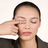 A young woman wearing a sparkly moissanite eternity ring on her index finger covering her left eye with her index finger.