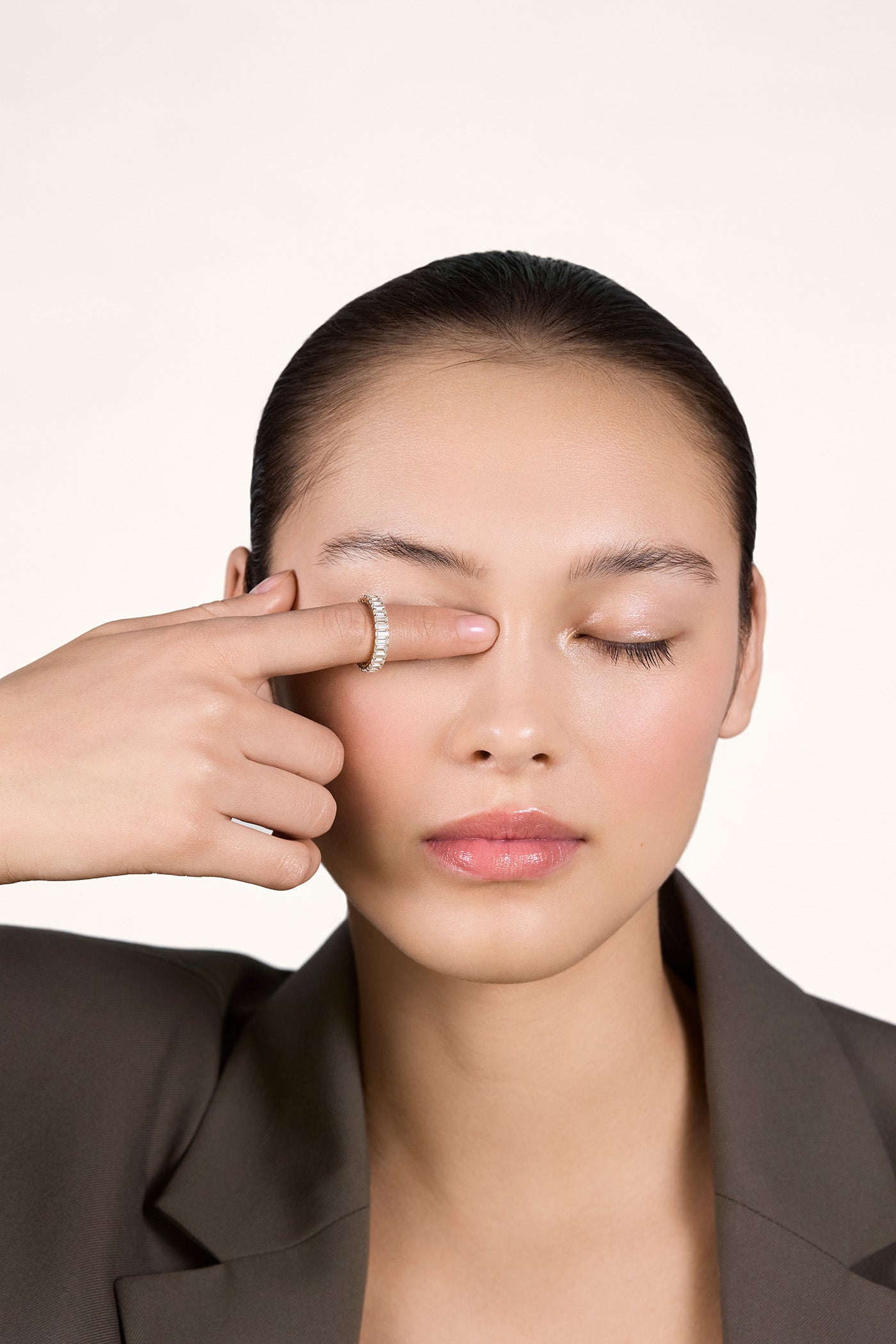 A young woman wearing a sparkly moissanite eternity ring on her index finger covering her left eye with her index finger.