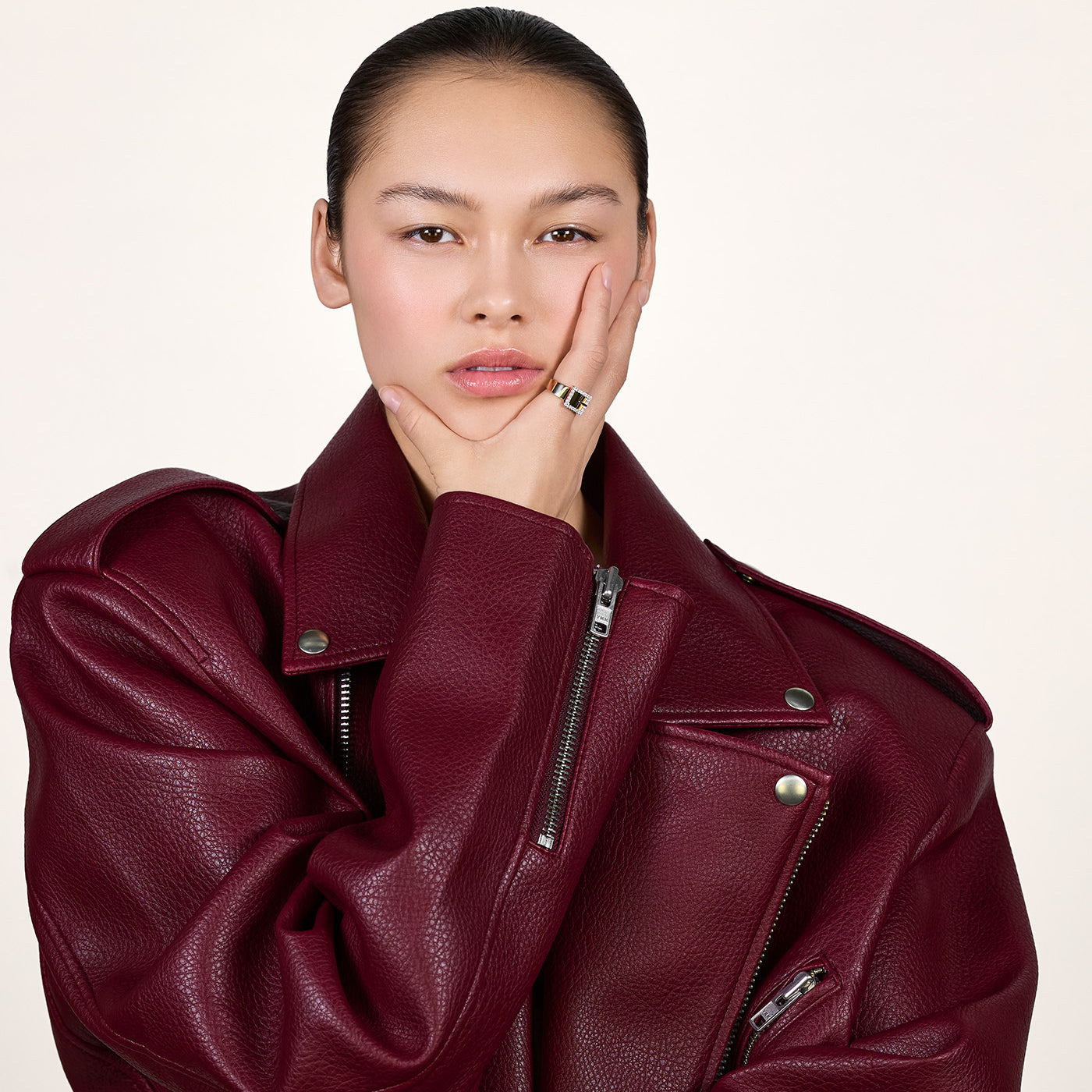 A young woman wearing a burgundy red leather jacket and wearing a gold ring on her index finger.