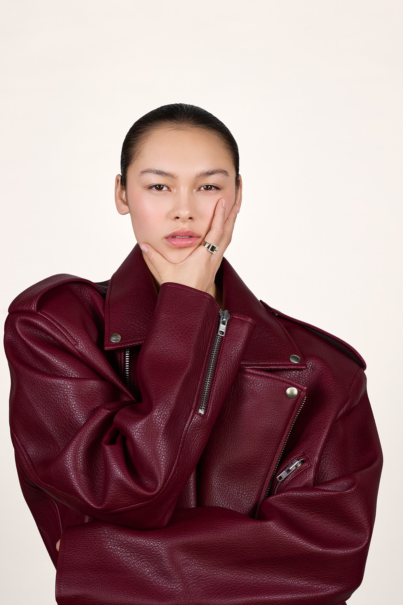 A young woman wearing a burgundy red leather jacket and wearing a gold ring on her index finger.