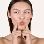 A young woman puckering her lips while holding her two index fingers beside her mouth, with one finger wearing the Eliana 2mm Eternity Ring featuring lab-grown diamonds