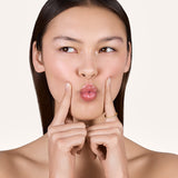 A young woman puckering her lips while holding her two index fingers beside her mouth, with one finger wearing the Eliana 2mm Eternity Ring featuring lab-grown diamonds