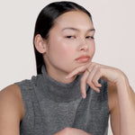 A video of a young woman wearing a grey turtleneck sweater without sleeves and wearing a gold ring on her middle finger.