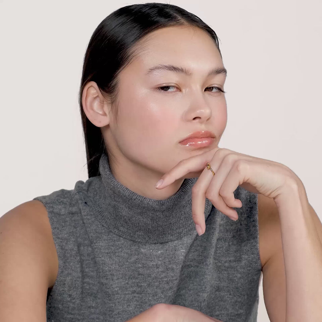 A video of a young woman wearing a grey turtleneck sweater without sleeves and wearing a gold ring on her middle finger.