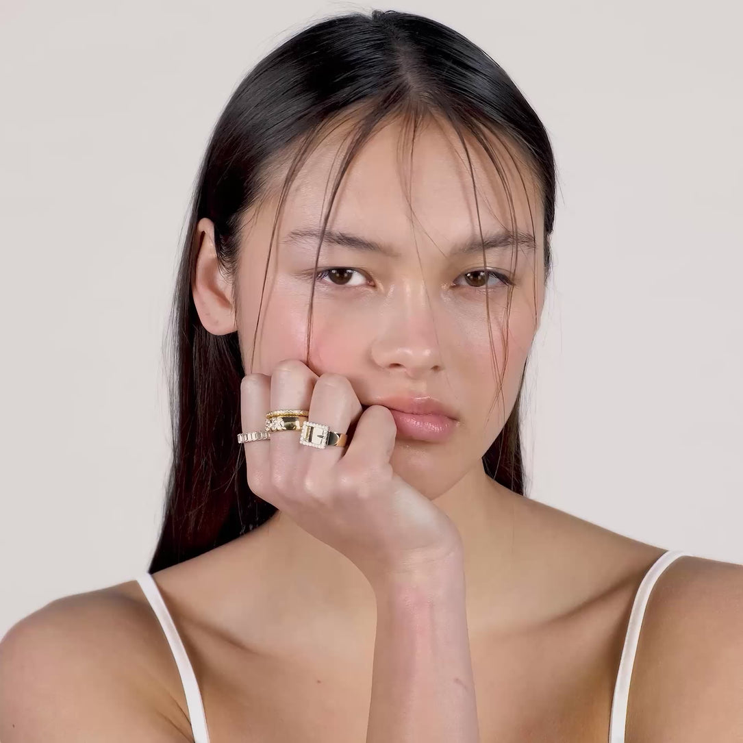 A video of a young woman with strands of hair in her face wearing multiple gold rings on her fingers.