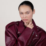 A video of a young woman wearing a burgundy red leather jacket and wearing a gold ring on her index finger.