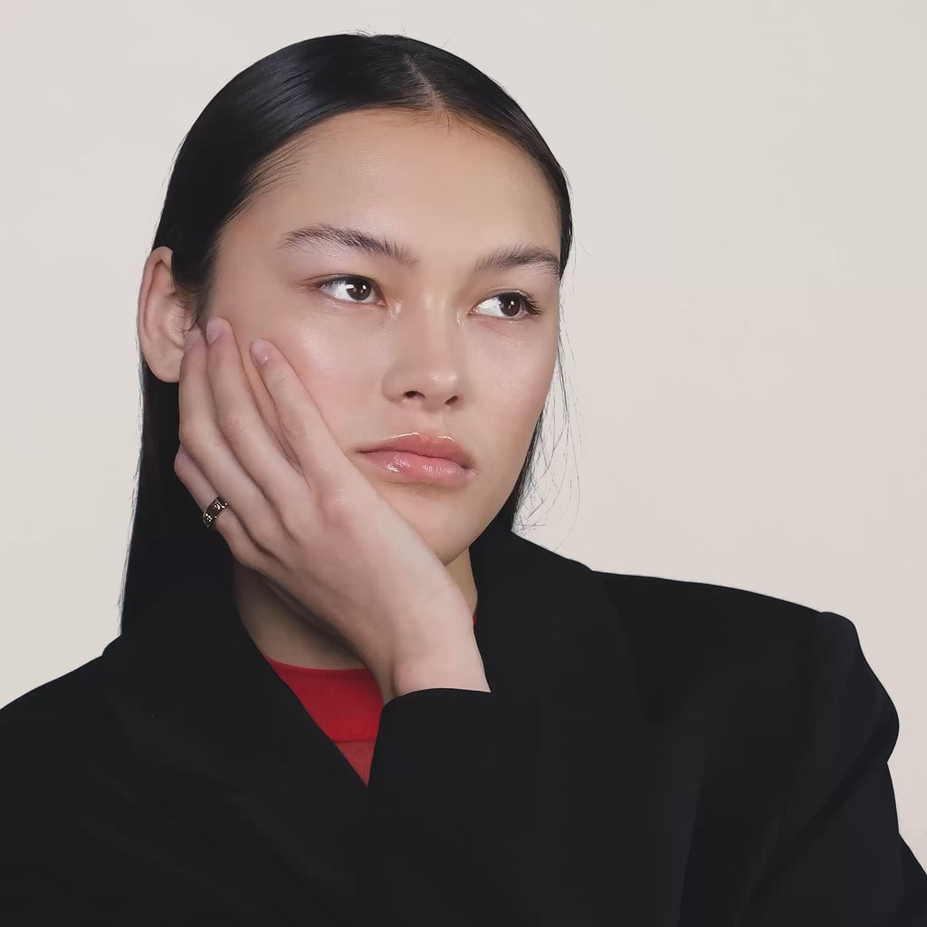 A video of a young woman wearing a black blazer and wearing a gold ring on her index finger.